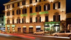 A multi-story hotel with a classic facade, illuminated signage, and a street view with passing vehicles. - c-hotels Club (Florence)