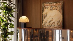 A modern room with a reflective console table, a potted plant, a lamp, and a large abstract painting on the wall. - c-hotels Club (Florence)