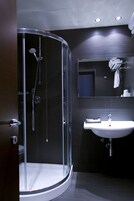 Een moderne badkamer met een douche met glazen wand, een witte wastafel en een spiegel boven de wastafel.