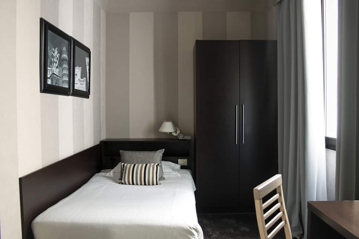 A hotel room with a bed, a nightstand, a lamp, a wardrobe, and a chair.