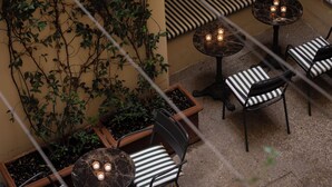 A terrace with striped seating, tables with candles, and a wall covered in climbing plants. - c-hotels Club (Florence)