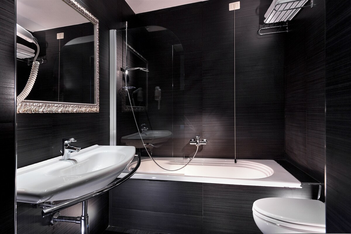 A modern bathroom with a large mirror, two sinks, a bathtub, and a toilet.