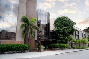 A modern hotel with a reflective glass facade, a prominent entrance with a sign, and lush greenery around the property. - Carppa Hotel (Fortaleza)