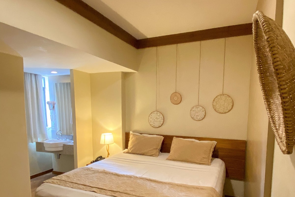 Une chambre d’hôtel avec un grand lit, un plancher en bois, une table de chevet avec une lampe et une fenêtre avec des rideaux.