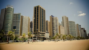 A cityscape with high-rise buildings, palm trees, and a sandy beach. - Magna Praia Hotel (Fortaleza)