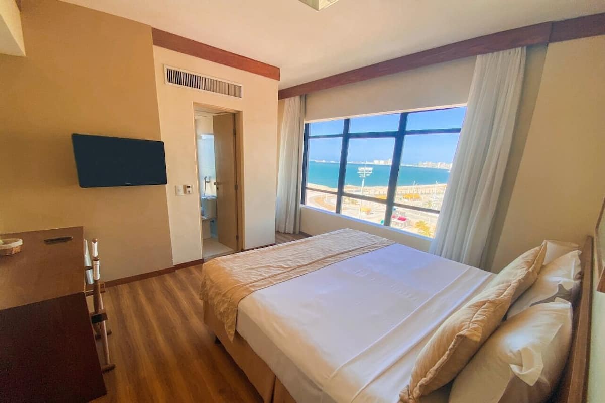 Une chambre d’hôtel avec un grand lit, une télévision, un plancher en bois et une vue sur la mer.