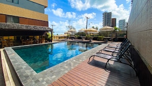 A swimming pool with lounge chairs and umbrellas, surrounded by buildings and a clear sky. - Magna Praia Hotel (Fortaleza)