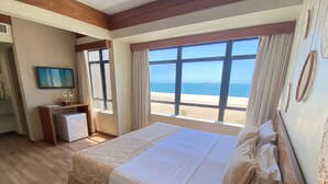 A hotel room with a large bed, a desk, a television, and a view of the beach. - Magna Praia Hotel (Fortaleza)