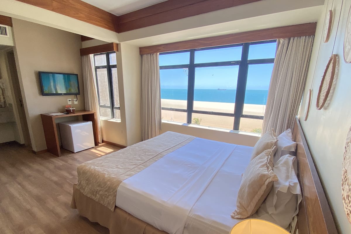 Une chambre d’hôtel avec un grand lit, un bureau, une télévision et une vue sur la plage.