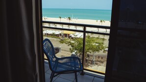 A balcony with a view of a beach, a chair, and a dining area with umbrellas. - Afago Mareiro Hotel (Fortaleza)