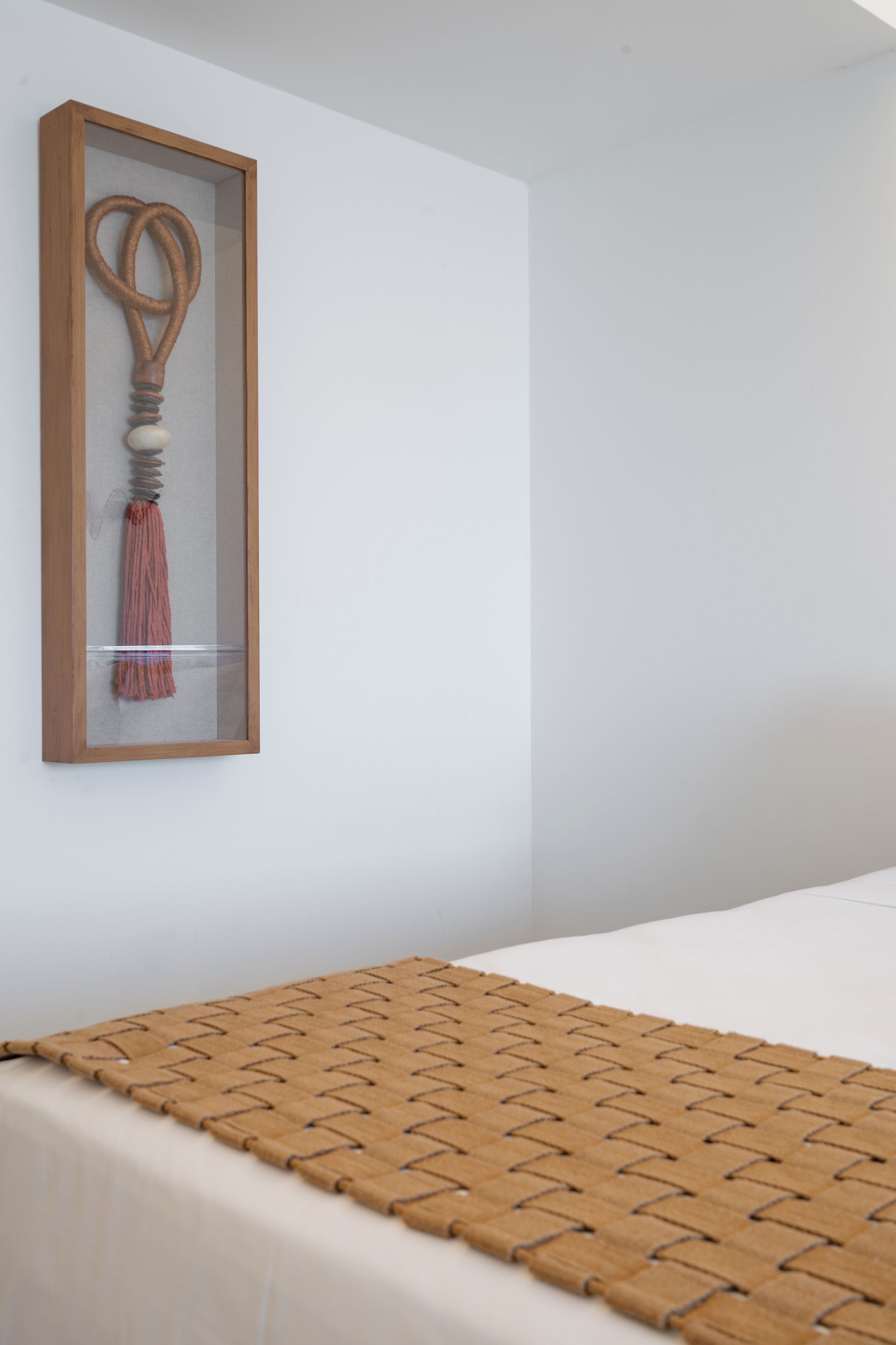 Una habitación con una cama, un objeto enmarcados en la pared y una manta tejida sobre la cama.