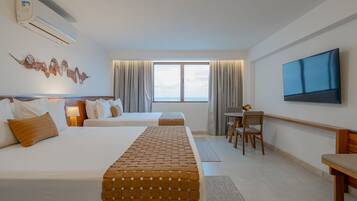 Quarto de hotel com duas camas, televisão, janela com cortinas e vista para o mar.