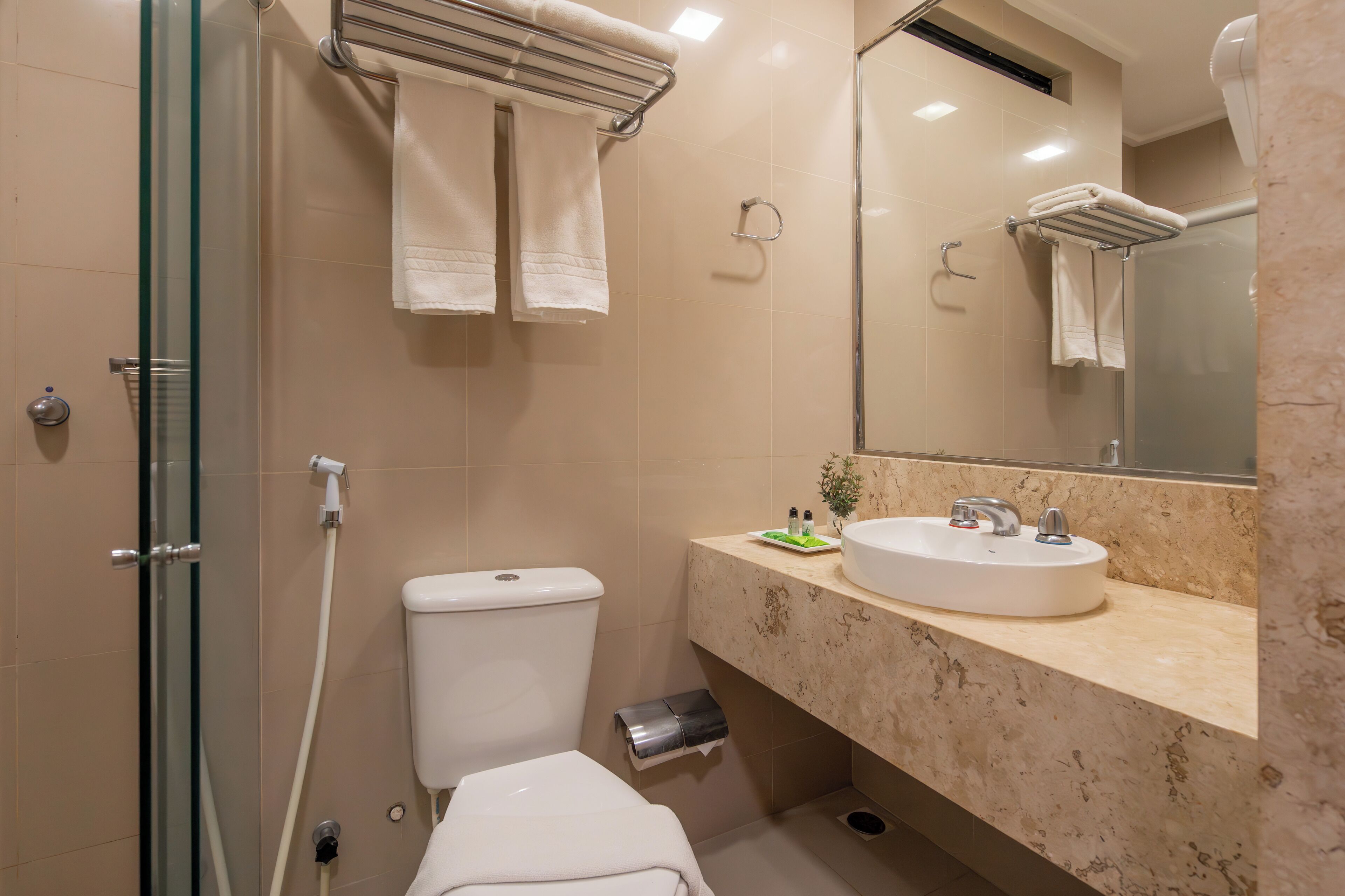 Un baño moderno con cabina de ducha de vidrio, inodoro, lavabo con encimera de mármol y espejo sobre el lavabo.