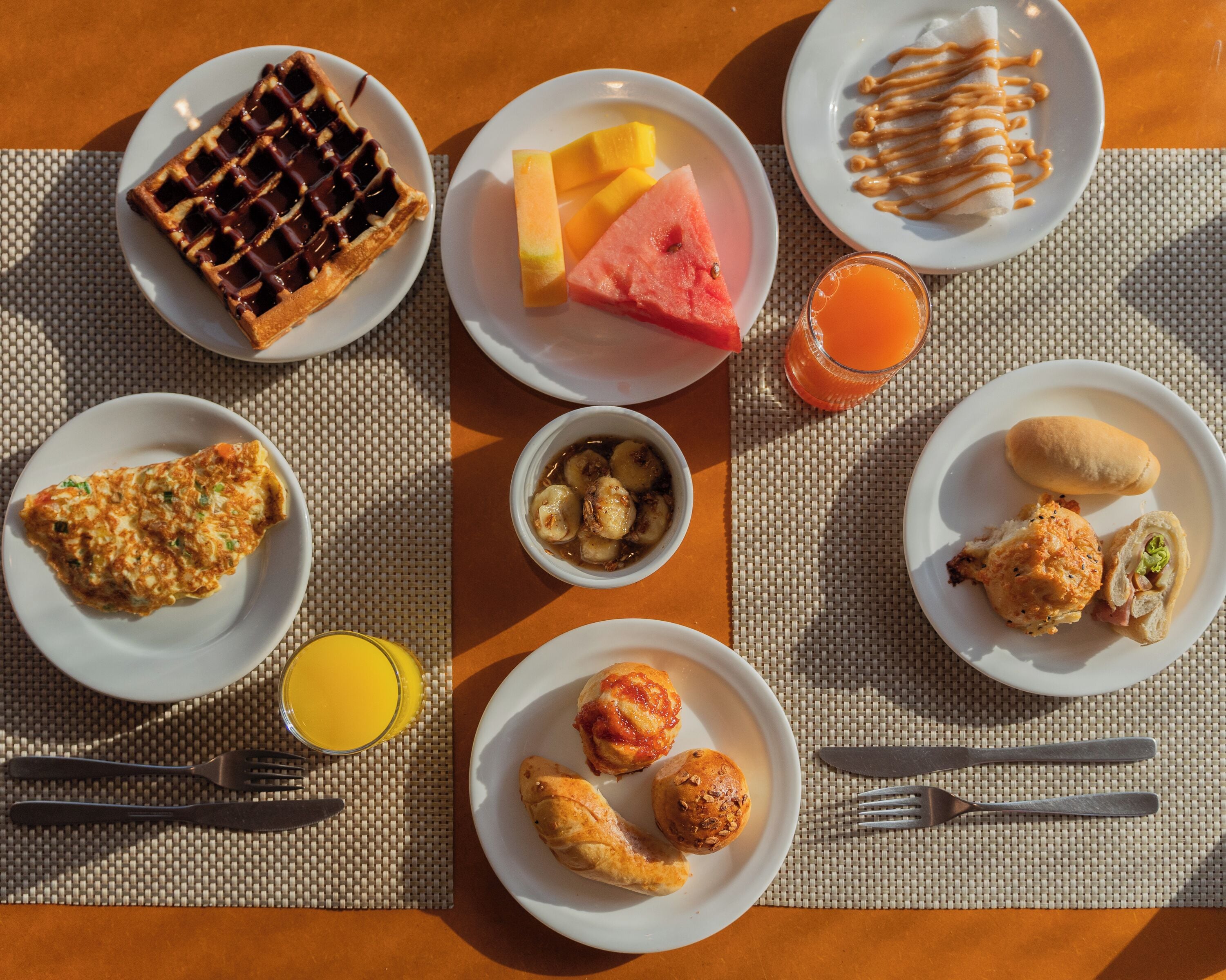 A breakfast setting with waffles, fruit, pastries, and a glass of orange juice on a table.