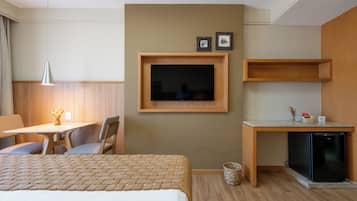 A hotel room with a bed, a desk, a chair, a television, and a small refrigerator.