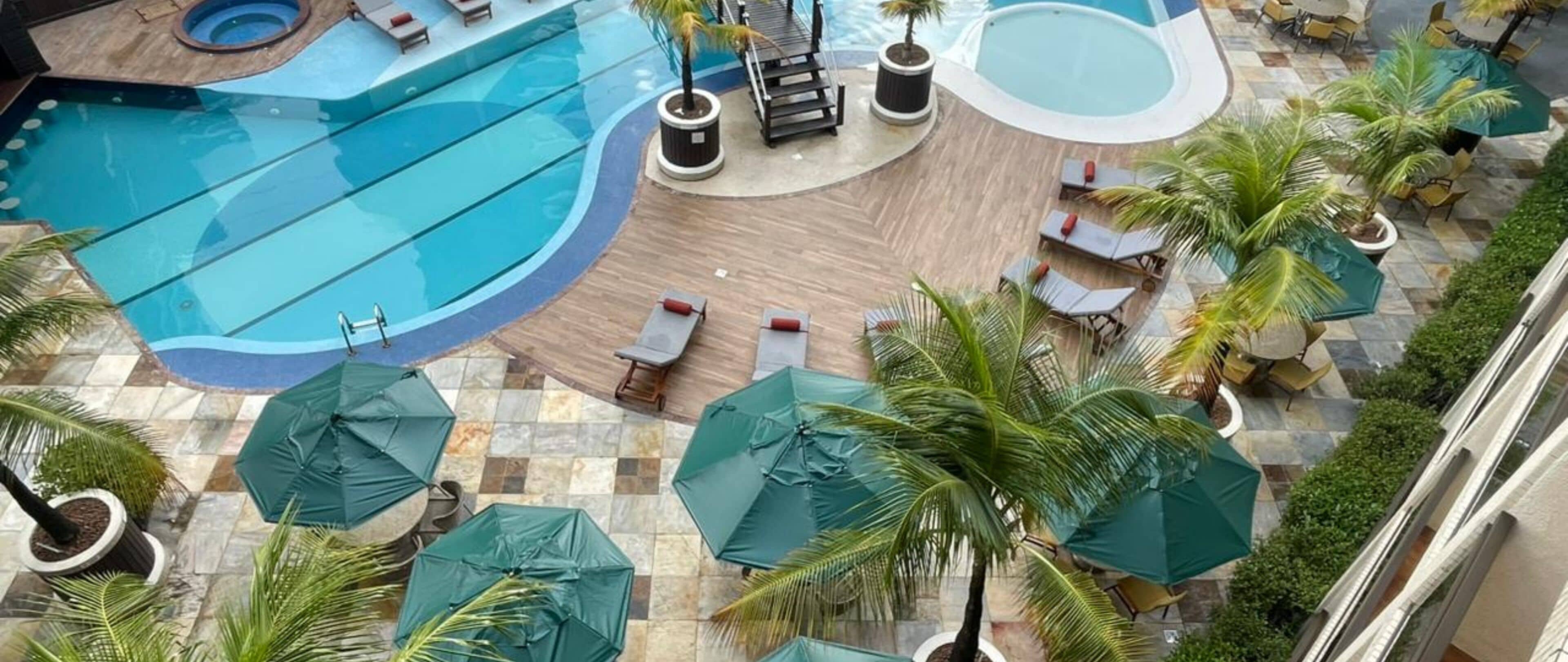 Un espace piscine aménagé sur le toit, avec des chaises longues, des parasols et des palmiers.
