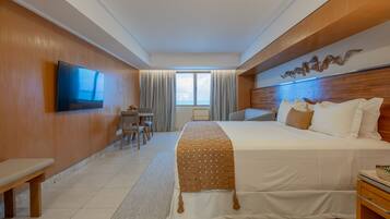 A hotel room with a large bed, a TV mounted on the wall, a small table with chairs, and a window with curtains.