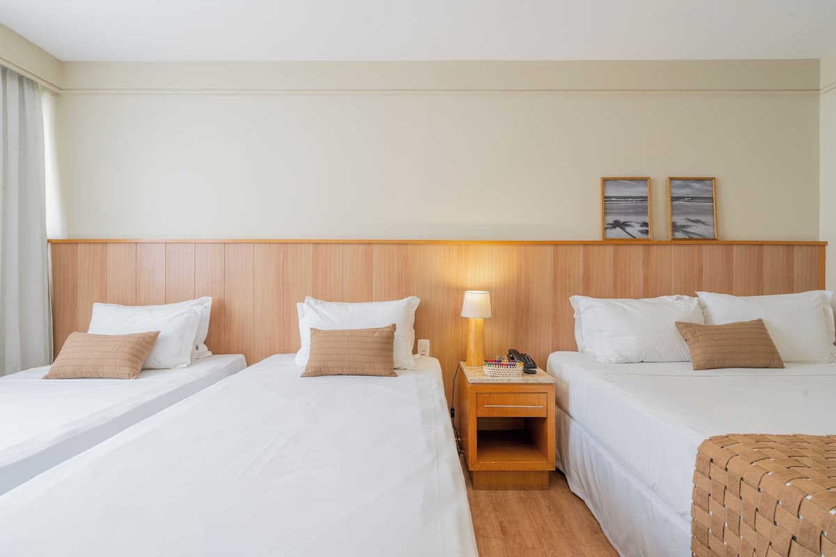 A hotel room with two beds, a wooden headboard, a nightstand with a lamp, and two framed pictures on the wall.