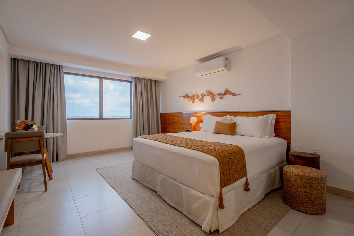 A hotel room with a large bed, a desk, a chair, and a view of the sky through a window.