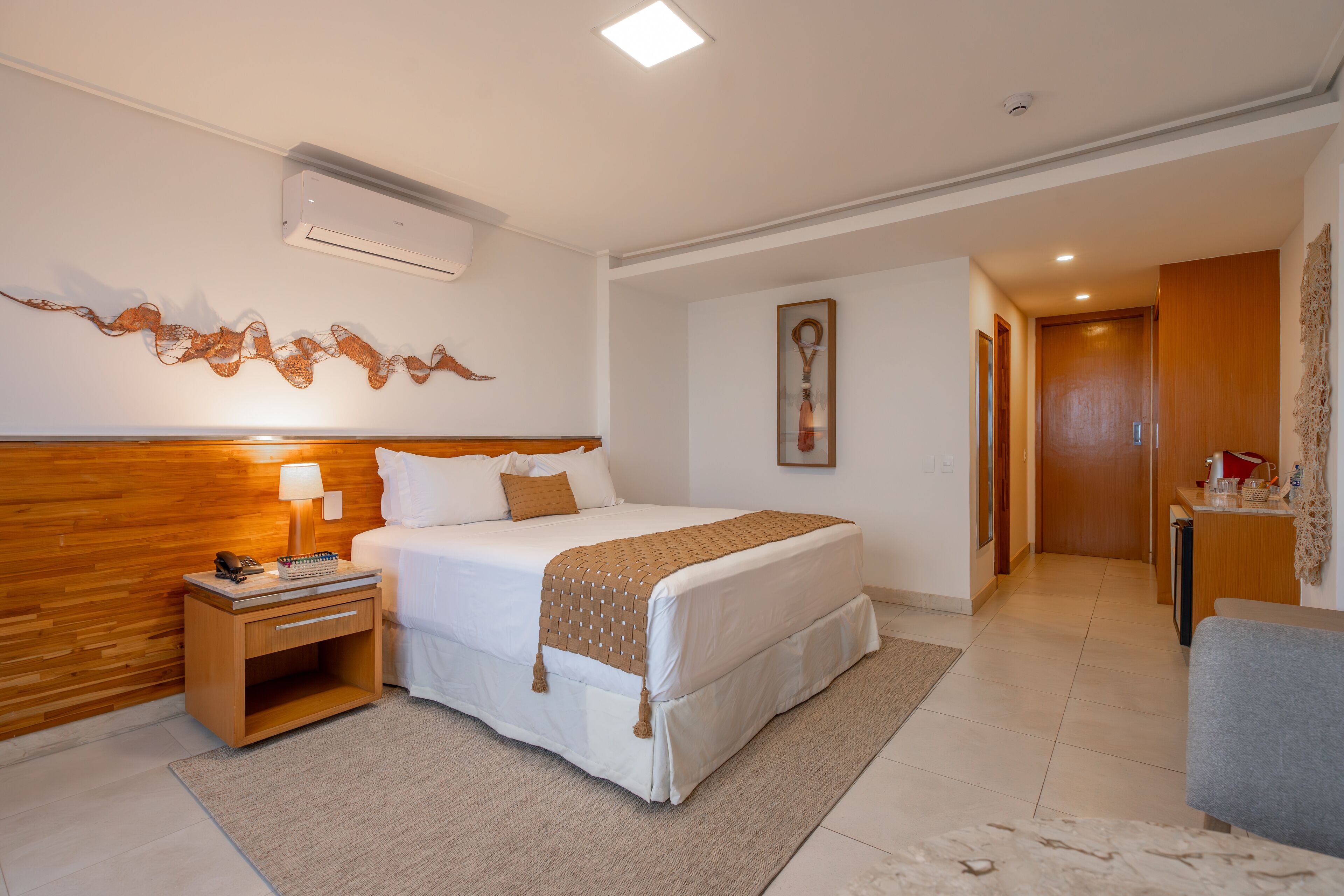 Habitación de hotel con una cama grande, mesita de noche, lámpara y aire acondicionado instalado en la pared.