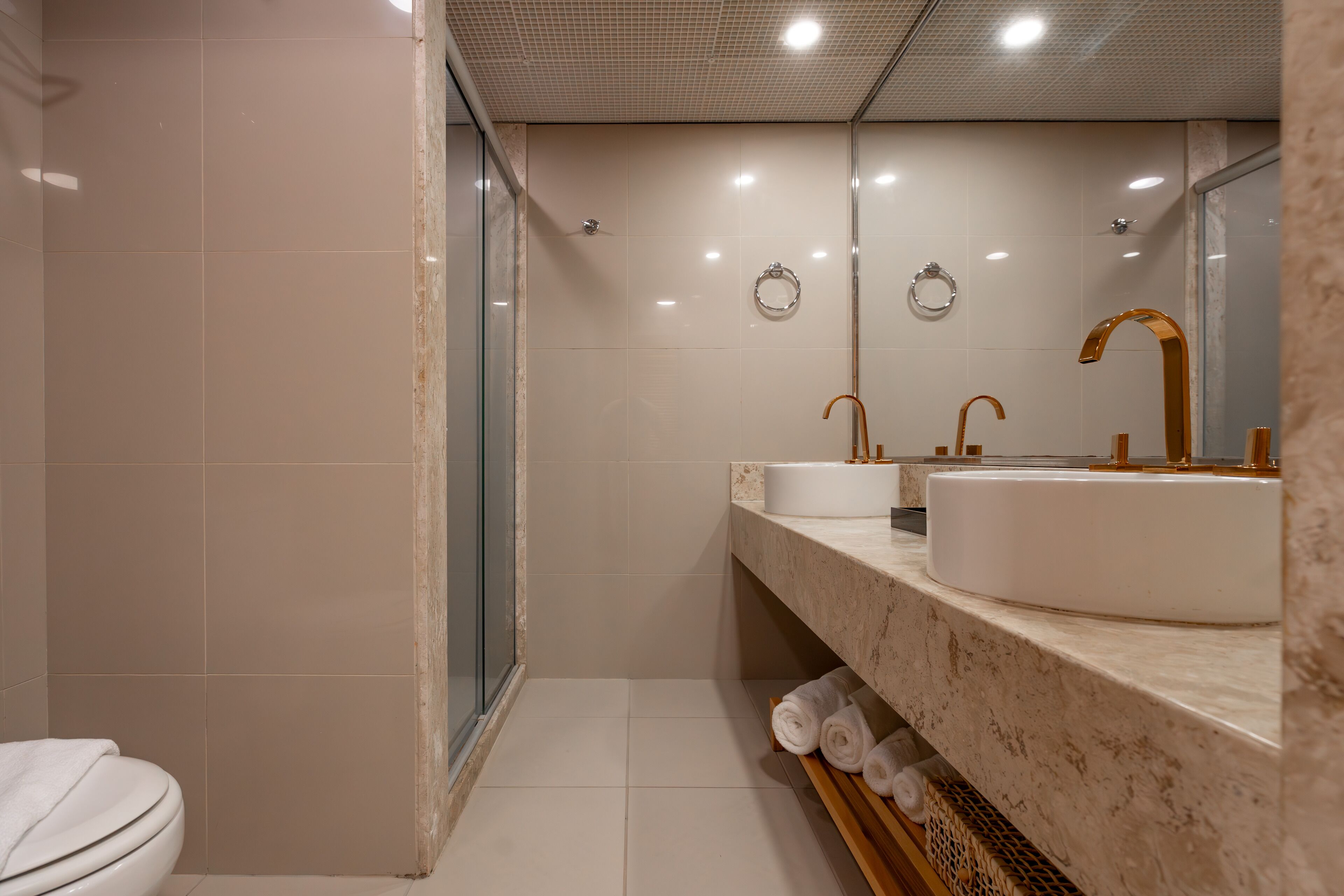 Un baño moderno con cabina de ducha de vidrio, inodoro blanco y encimera de mármol con dos lavamanos.