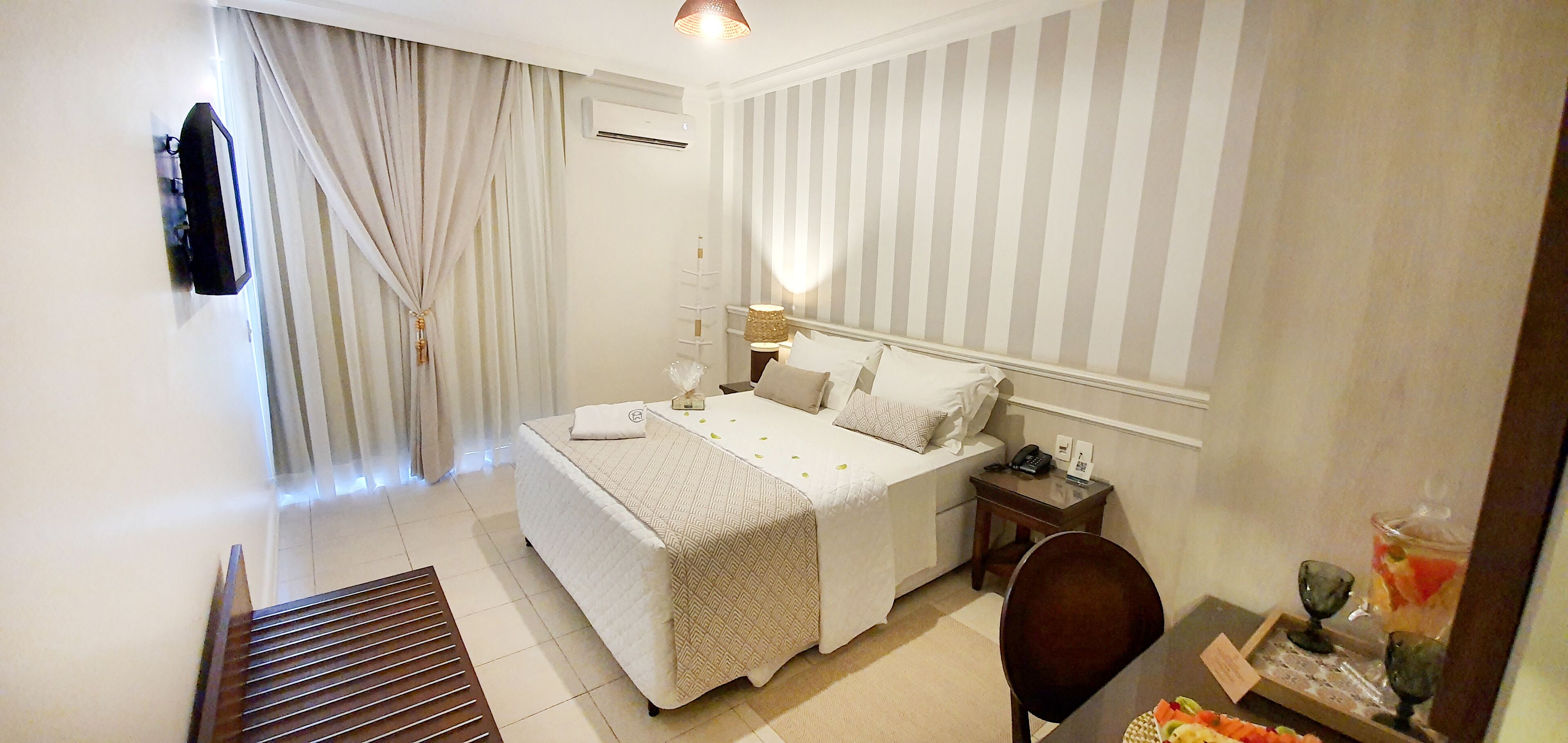 Una habitación de hotel con cama, mesita de noche, lámpara y una pequeña mesa con frutero.