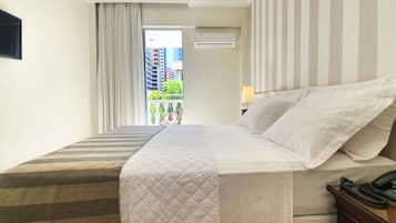 A hotel room with a bed, a telephone, and a view of a balcony with plants and buildings.