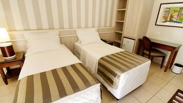 A hotel room with two beds, a desk, a chair, a lamp, and a refrigerator.