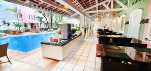 Un espace bar aménagé au bord de la piscine, avec un comptoir, des chaises et des tables.