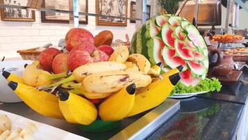 Una exhibición de frutas con plátanos, manzanas y una sandía tallada con forma de flor.