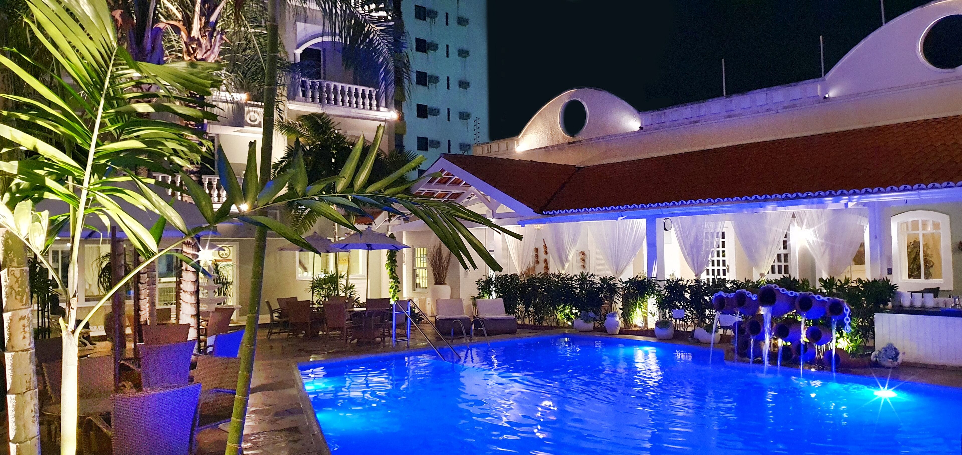 A pool area with chairs and umbrellas, surrounded by plants and a building with a balcony.