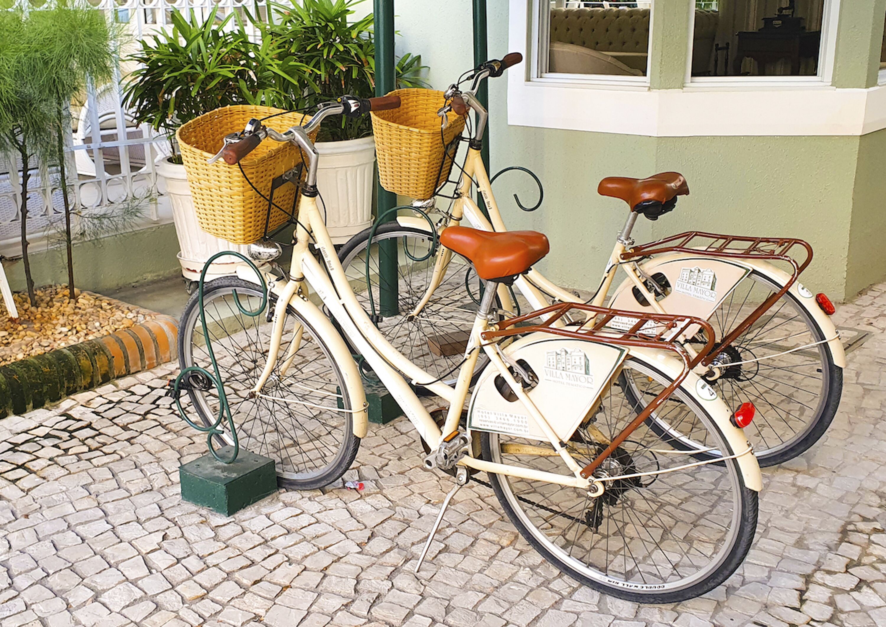 Una bicicleta antigua con cestas de mimbre y un asiento de cuero marrón estacionada sobre pavimento adoquinado.