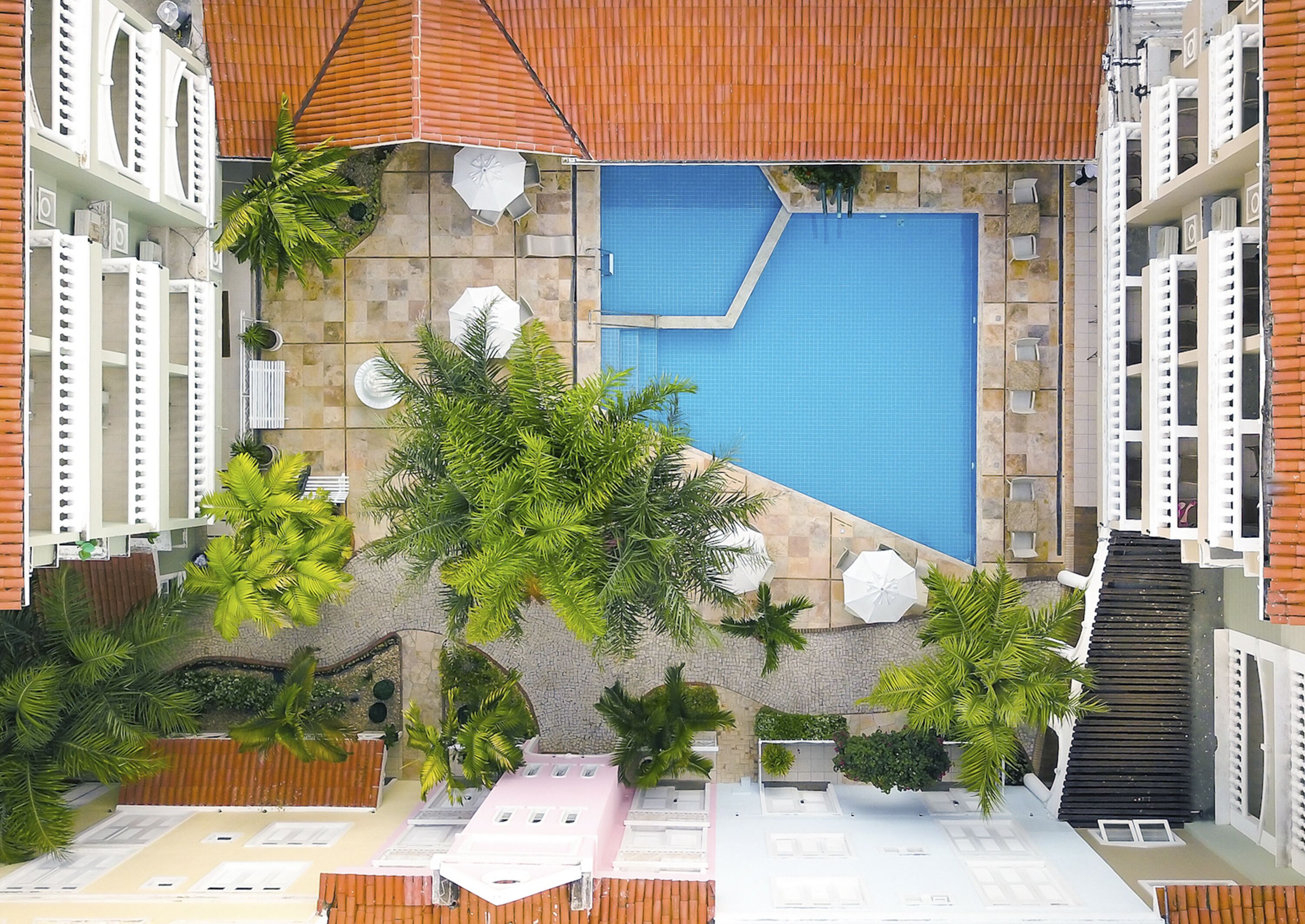 Uma área de piscina no terraço com piscina azul, rodeada por plantas em vasos e mobiliário para área externa.