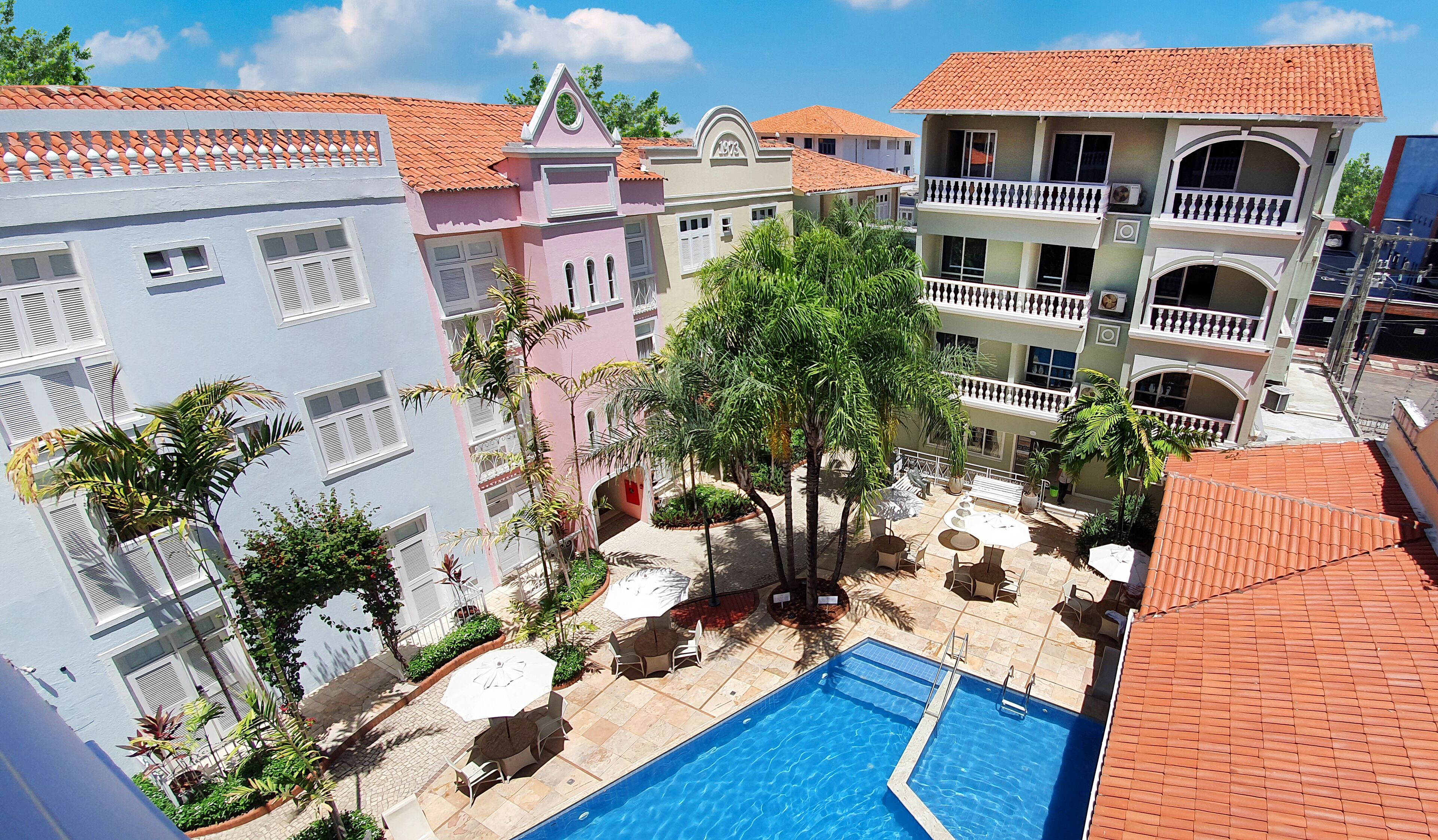 A multi-story building with a swimming pool, outdoor seating, and a garden area.