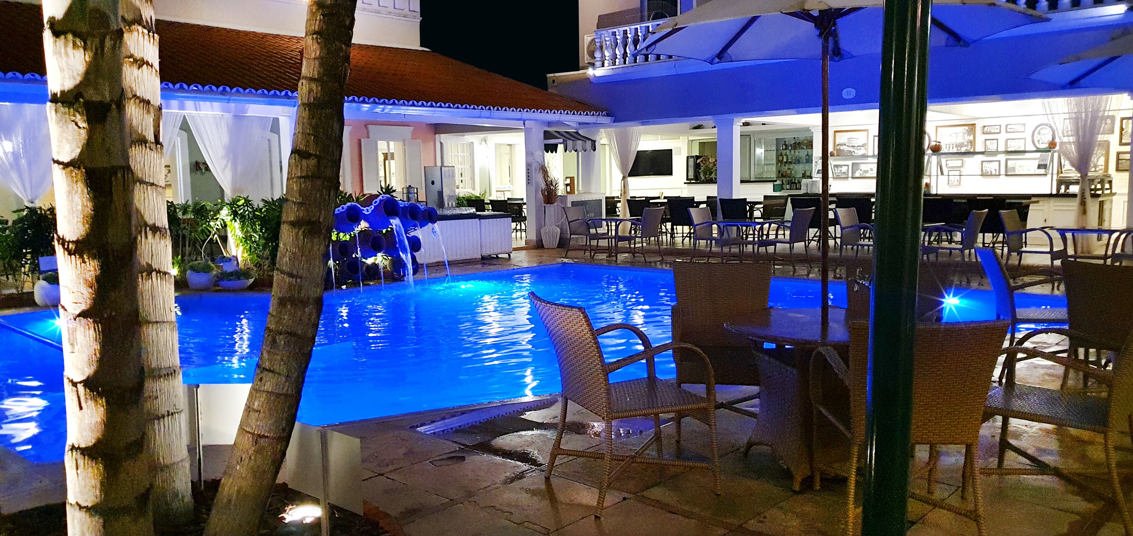 Un espace extérieur avec une piscine, des chaises et des tables, entouré de palmiers et comprenant un bar.