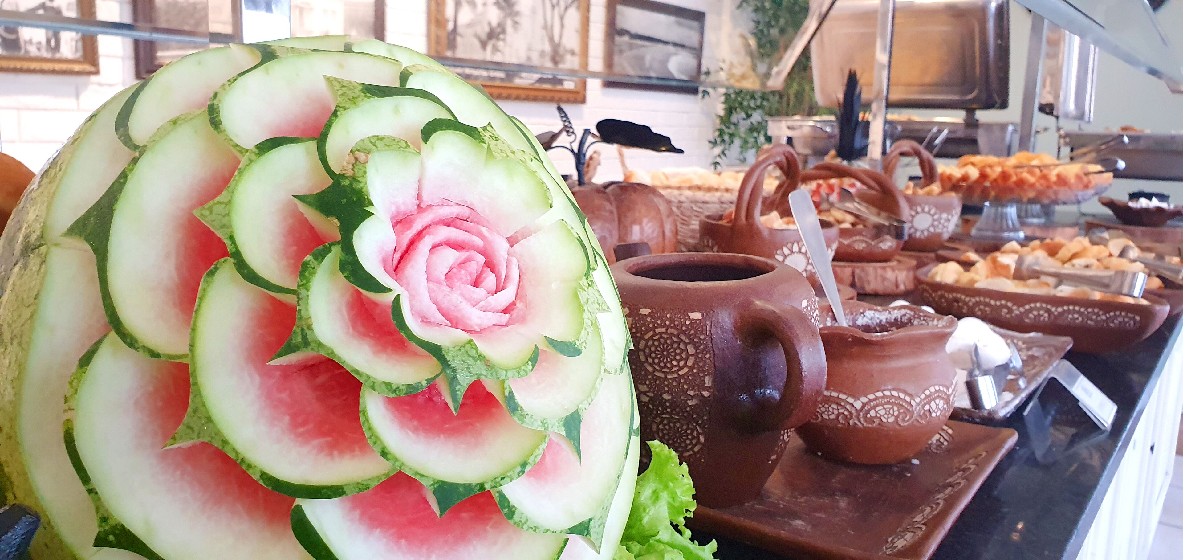 A watermelon carved into a rose with a teapot and bread on a table.