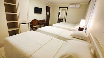 Quarto de hotel com duas camas, uma escrivaninha, uma cadeira, uma televisão e um guarda-roupa.