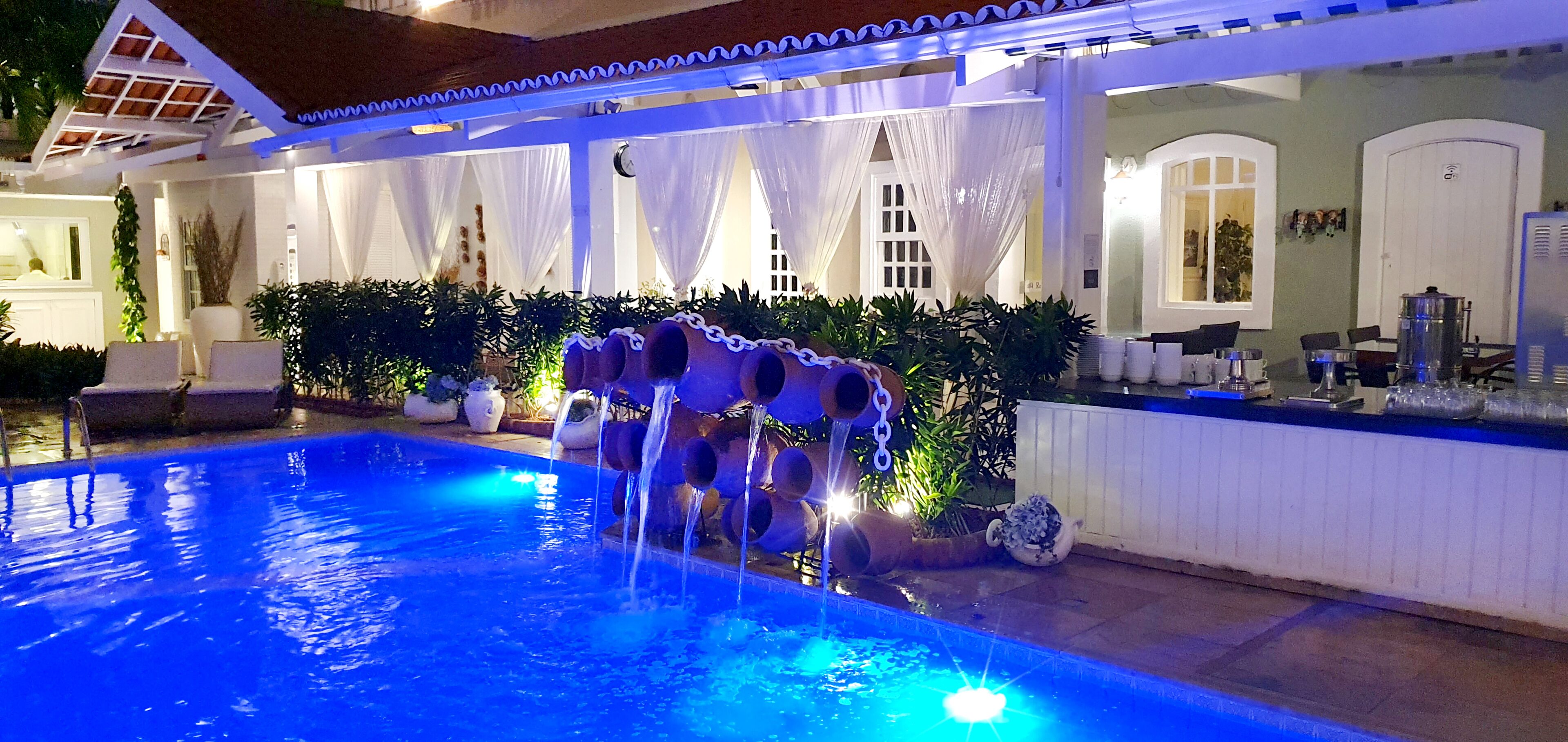 Ein Pool mit Wasserspiel, umgeben von Pflanzen und einem überdachten Sitzbereich.