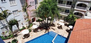 Un espace piscine aménagé sur le toit, doté de plusieurs chaises longues et de parasols, entouré de palmiers et d’une piscine.