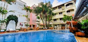 Une piscine entourée de bâtiments à plusieurs étages dotés de balcons, avec des chaises longues et des parasols à proximité.