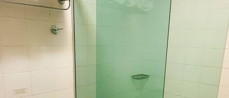 A bathroom with a glass-enclosed shower, a toilet, and a shelf with rolled towels.