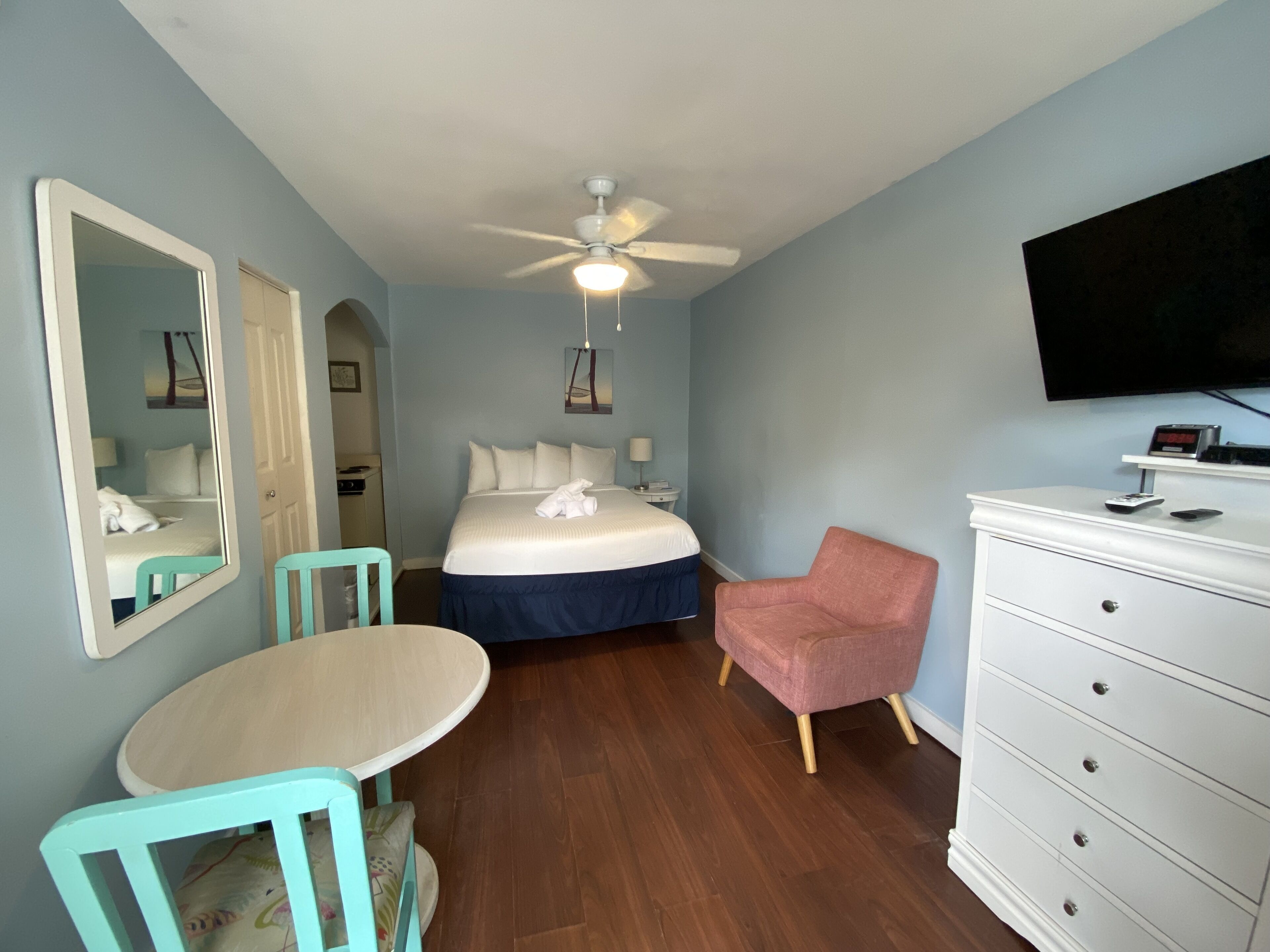 A hotel room with a bed, a desk, a chair, a dresser, a ceiling fan, and a TV.