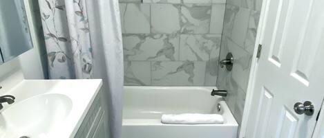 A bathroom with a bathtub, a shower, a sink, and a mirror.