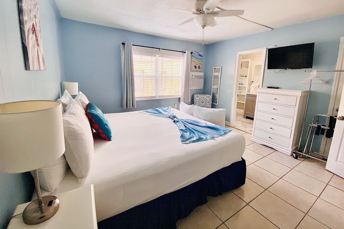 A bedroom with a bed, a ceiling fan, a window with curtains, a TV, and a dresser.