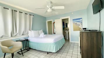 Habitación de hotel con cama, una silla, un escritorio, televisión y baño visible a través de una puerta abierta.
