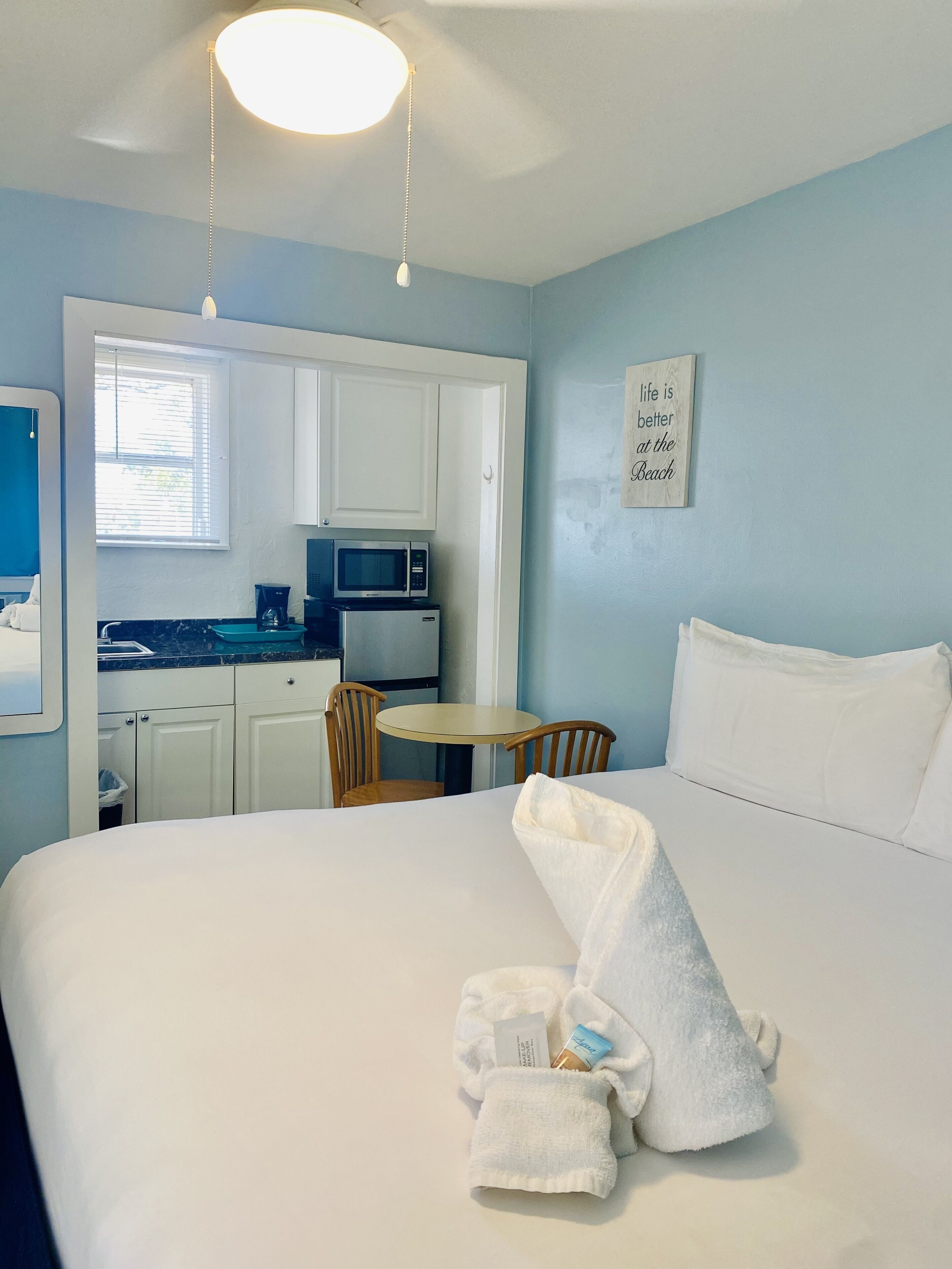 A hotel room with a bed, a small table, a chair, a microwave, and a kitchenette.