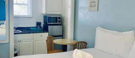 A hotel room with a bed, a small table, a chair, a microwave, and a kitchenette.