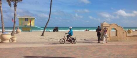 Un vialetto lastricato con palme, una spiaggia e un edificio con facciata gialla.