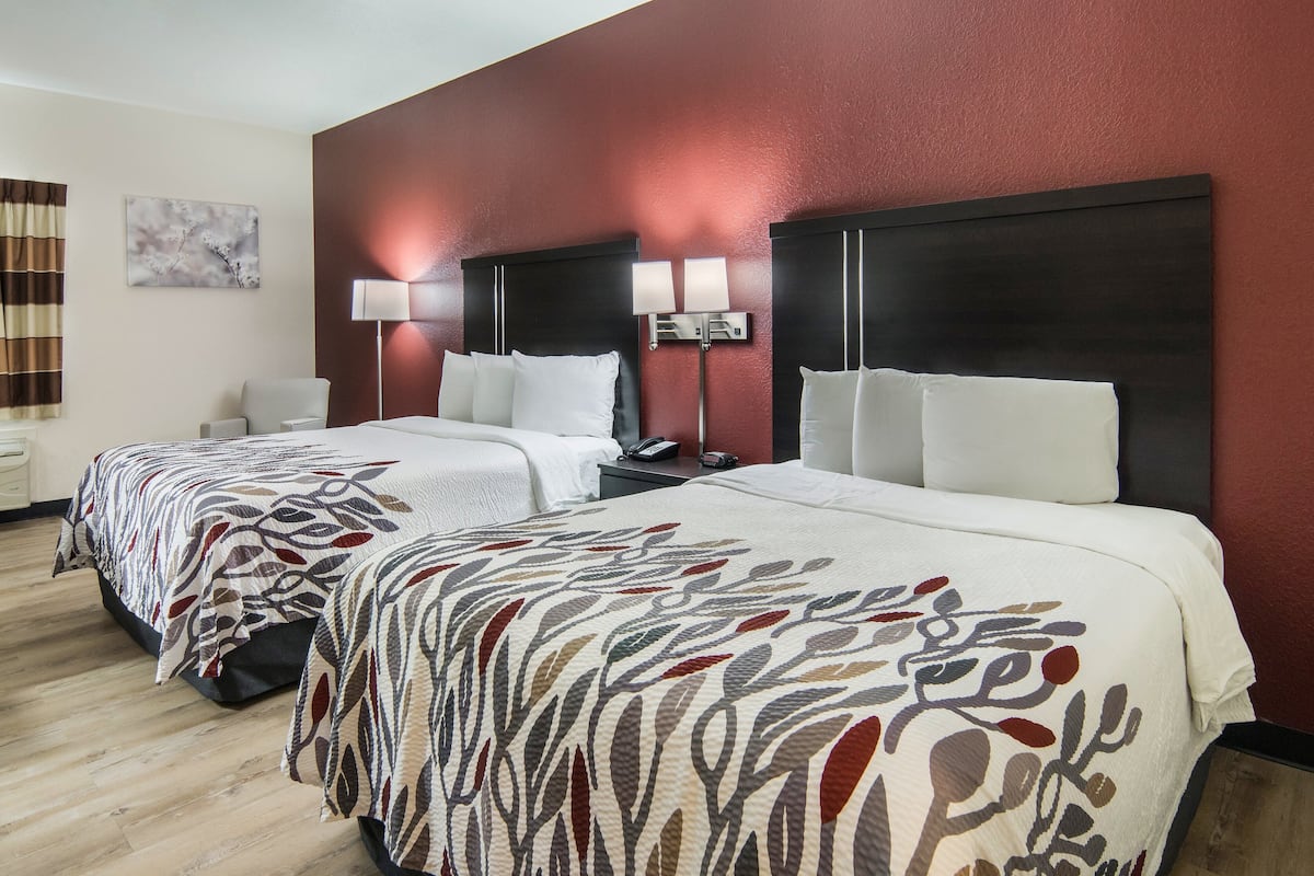 A hotel room with two beds, a nightstand, a lamp, and a painting on the wall.