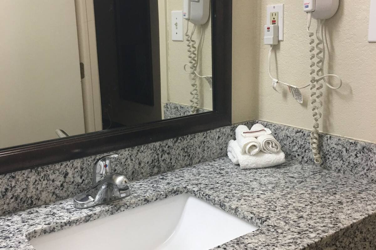 A bathroom with a granite countertop sink, a mirror, and a hair dryer mounted on the wall.